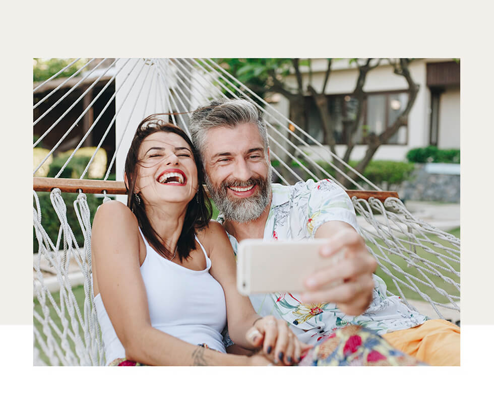 An older couple taking a selfie in a hammock